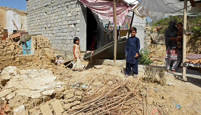 A woman and her children stand beside their collapsed mud house following an earthquake in the remote mountainous district of Harnai on October 7, 2021, as at least 20 people were killed and dozens injured when a shallow earthquake hit southwestern Pakistan in the early hours of October 7. — AFP