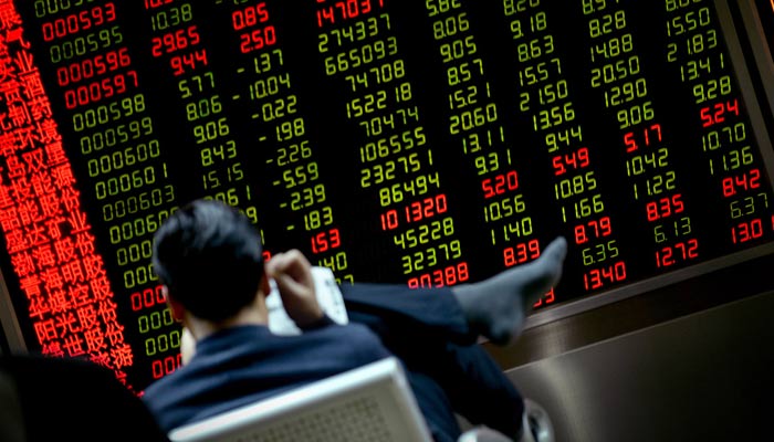 This photo taken on January 20, 2016 shows an investor reading a newspaper in front of a screen showing stock market movements at a securities company. — AFP/File