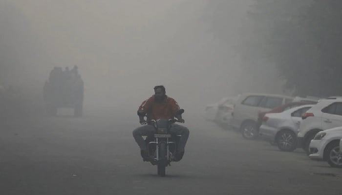 Seorang pria mengendarai sepeda motor di sepanjang jalan yang diselimuti kabut asap di Noida, India, 5 November 2021. Foto: Reuters