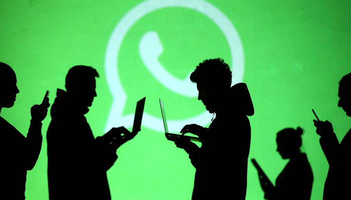 Silhouettes of laptop and mobile device users are seen next to a screen projection of Whatsapp logo in this picture illustration taken March 28, 2018. Reuters/File