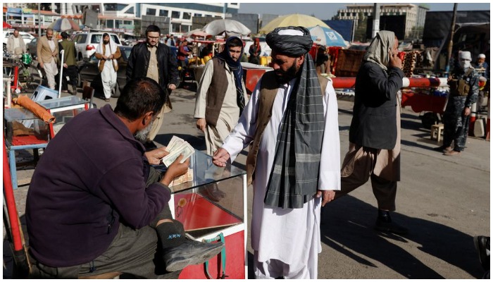 An Afghan currency exchange dealer checks banknotes in front of a man at the market in Kabul, Afghanistan October 24, 2021. REUTERS/Stringer