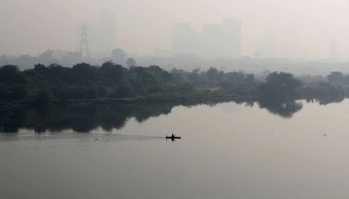 Seorang pria mendayung perahu saat bangunan diselimuti kabut asap terlihat di latar belakang di pinggiran Delhi, India, 15 November 2021. — Reuters
