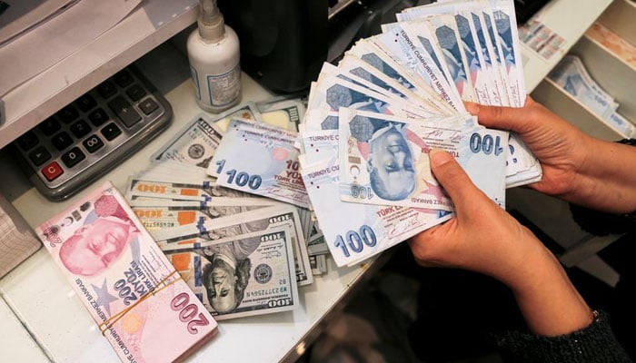 Seorang penukar uang memegang uang kertas lira Turki di kantor penukaran mata uang di Ankara, Turki 12 Oktober 2021. — Reuters/File