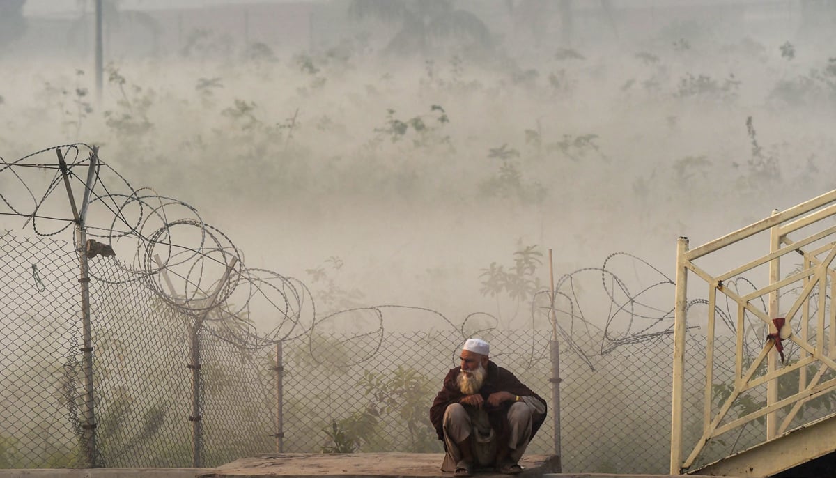 A man waits for transportation beside a street amid heavy smoggy conditions in Lahore on November 18, 2021. — AFP