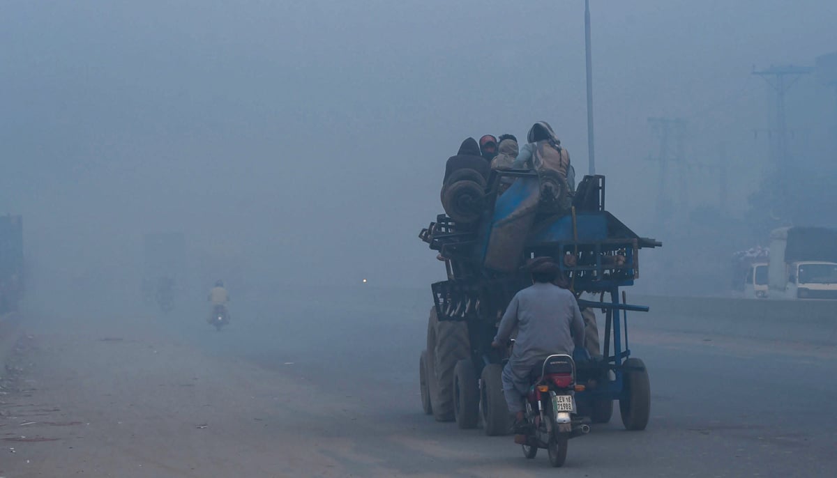 Orang-orang bepergian di sepanjang jalan di tengah kondisi kabut asap tebal di Lahore pada 18 November 2021. — AFP