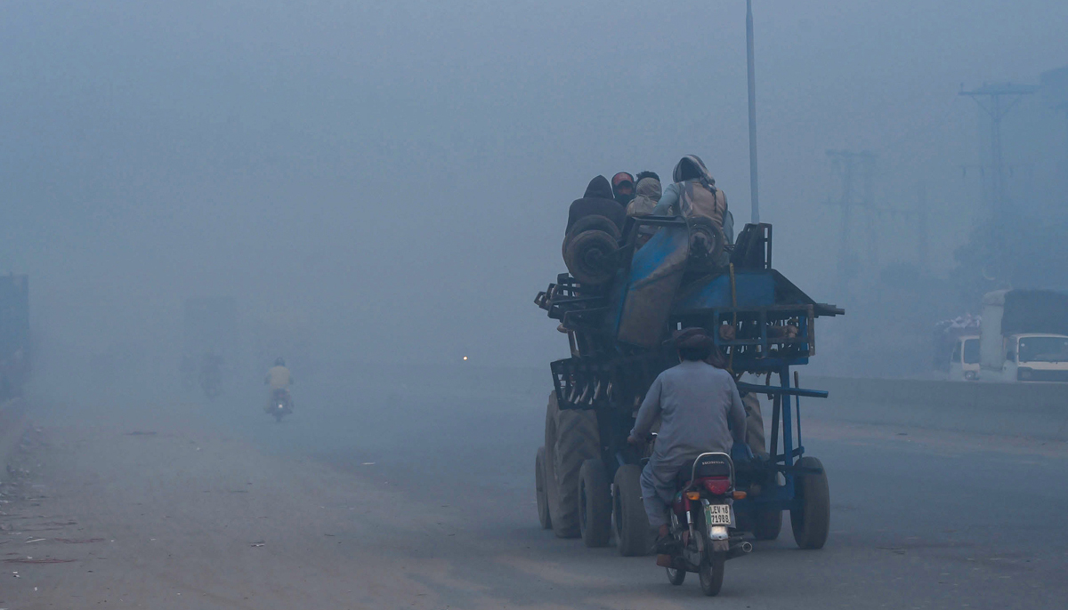 People commute along a street amid heavy smoggy conditions in Lahore on November 18, 2021. — AFP