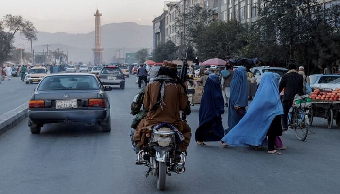 A group of women wearing burqas crosses the street as members of the Taliban drive past in Kabul, Afghanistan October 9, 2021. Photo: Reuters