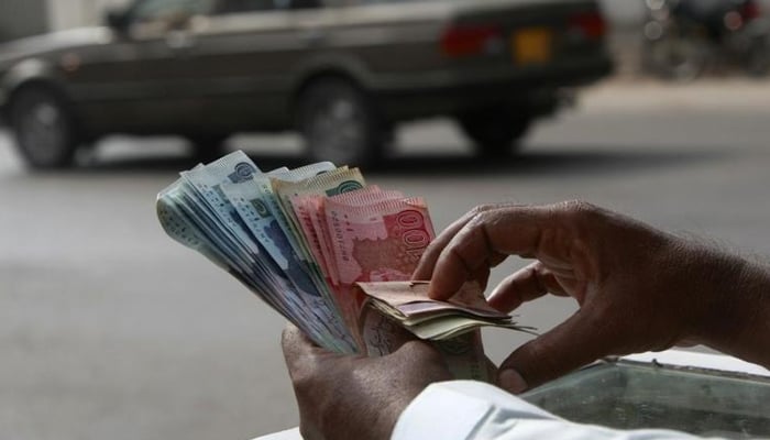 A money changer counts Pakistani Rupee (PKR) notes in Karachi September 23, 2009. — Reuters/File