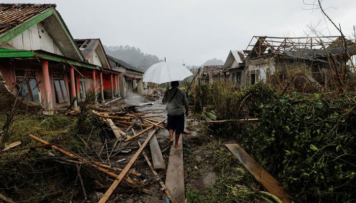 A man with an umbrella walks amongst damaged houses looking for his goat in an area affected by the eruption of Mount Semeru volcano in Curah Kobokan, Pronojiwo district, Lumajang, Indonesia, December 6, 2021. — Reuters
