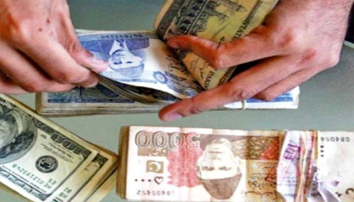 A currency dealer can be seen counting Rs1,000 Pakistani notes while stacks of Rs5,000 notes and $100 can be seen in this is AFP file photo.