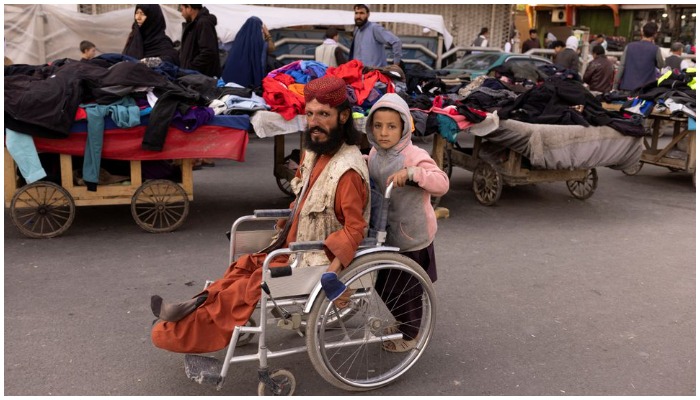 A boy pushes a mans wheelchair on a street in Kabul, Afghanistan, October 22, 2021. REUTERS/Jorge Silva