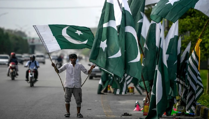 A vendor holds a Pakistani flag as he waits for customers beside his stall alongside a street in Islamabad. Photo: AFP