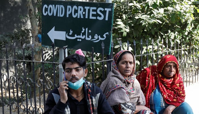 People sit next to a coronavirus disease (COVID-19) test sign outside the School of Nursing in Jinnah Postgraduate Medical Centre (JPMC), in Karachi, Pakistan December 9, 2021. — Reuters/File