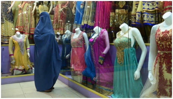 A burqa clad woman stands before headless mannequins at a shop. — AFP