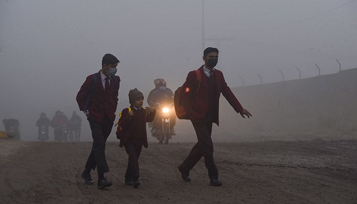 Children walk to their school along a street amid smoggy conditions early in the morning in Lahore on December 17, 2021. — AFP/file