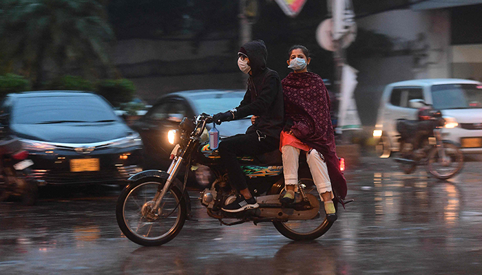 Commuters ride on a motorbike along a road during a rainfall in Karachi on January 4, 2022. — AFP/File