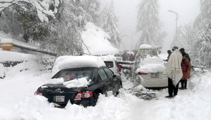 People stand next to cars stuck under fallen trees on a snowy road, in Murree, northeast of Islamabad, Pakistan in this still image taken from a video, January 8, 2022. — PTV/Reuters TV via Reuters