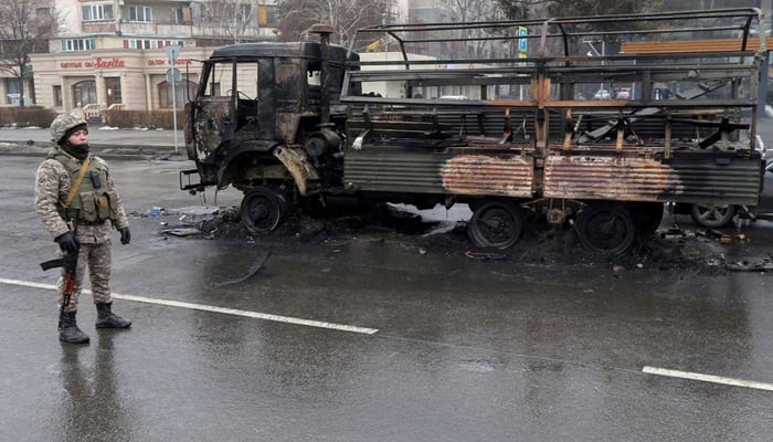 A Kazakh law enforcement officer stands guard near a burnt truck while checking vehicles in a street following mass protests triggered by fuel price increase in Almaty, Kazakhstan January 8, 2022. Photo: Reuters