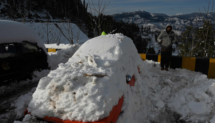 A man stands next to snow-covered card stucked on a road after a blizzard that started on January 7 and led to visitors being trapped in vehicles along the roads to the resort hill town of Murree, some 70 Kms northeast of Islamabad on January 9, 2022. — AFP