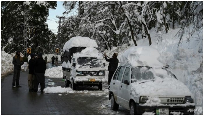 A man tries to clear snow off a vehicle on a road in Murree. — AFP