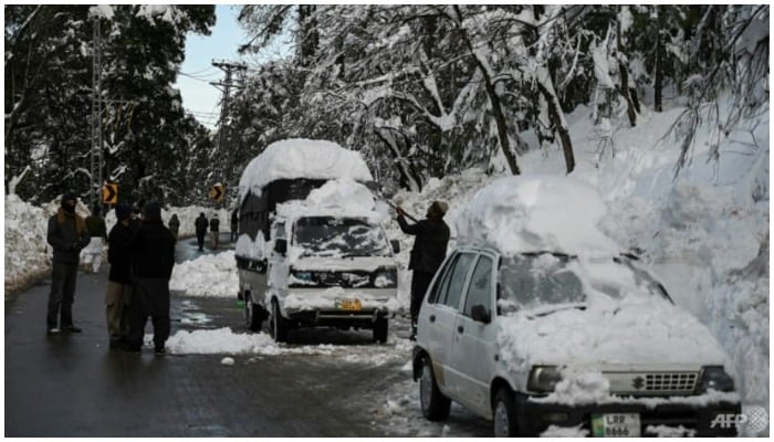 A man tries to clear snow off a vehicle on a road in Murree.— AFP