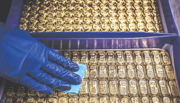 Person wearing rubber gloves wiping clean bars of gold — AFP