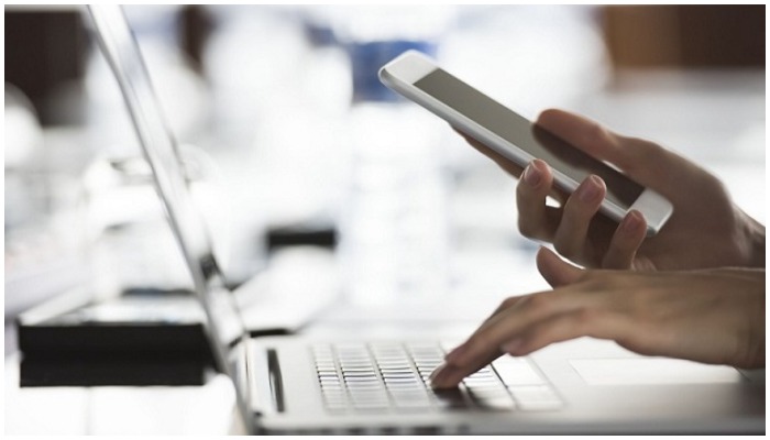 Representational image of a person holding a cellular phone and touching the keypad of a laptop — AFP/File