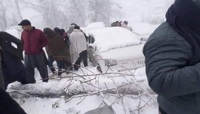 Image showing a car stranded in snow in Murree as people gather around it — Twitter