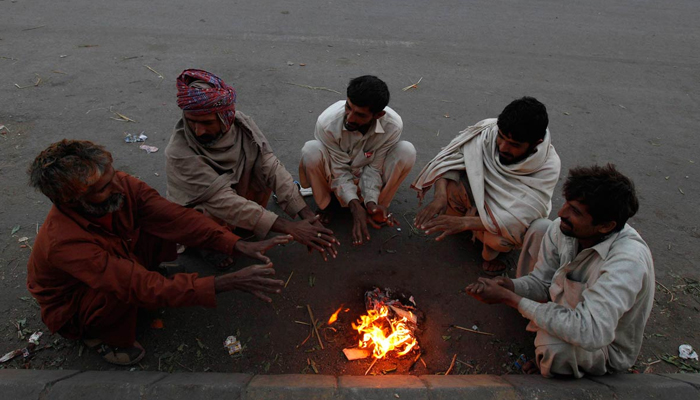 Fruit sellers sit around a fire to keep themselves warm during the early morning hours along a road in Karachi, Dec 30, 2013. — Reuters/File