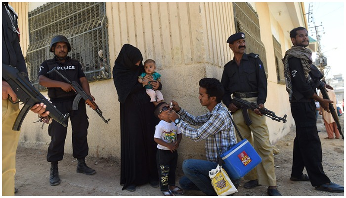Policemen stand guard as a health worker administers polio drops to a child during a polio vaccination campaign in Karachi. ─ AFP/ file