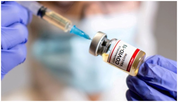 A person using a syringe to draw vaccine dose from a vile — Reuters