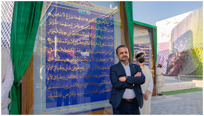 Shahid Rassam poses for a picture with a page of the Holy Quran at his back.