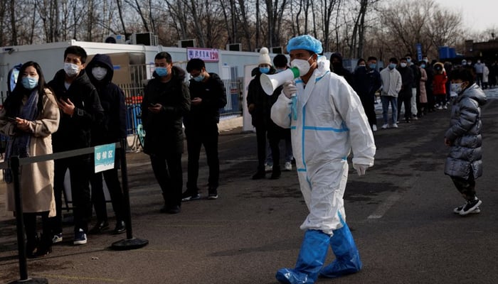 A staff member in a protective suit instructs people who are lining up for a throat swab test at a temporary COVID-19 testing center as the coronavirus disease (COVID-19) continues in Beijing, China, January 26, 2022. — Reuters