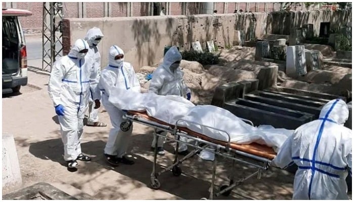 Paramedics dressed in Personal Protective Equipment carry a body on a stretcher inside a graveyard. Photo: Geo.tv/ file
