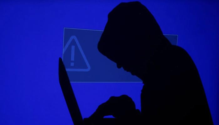 A hooded man holds a laptop computer as blue screen with an exclamation mark is projected on him in this illustration picture taken on May 13, 2017. — Reuters/File