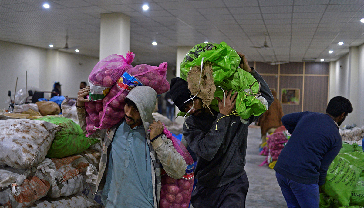 In this picture taken on January 8, 2022, workers of the Taza Transforming Agriculture carry vegetable bags at a distributing point in Lahore. — AFP