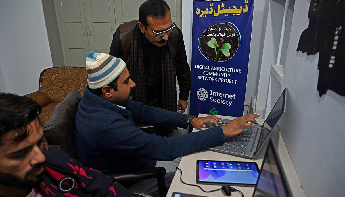In this picture taken on January 7, 2022, Aamer Hayat Bhandara, co-founder of Digital Dera, guides a farmer on how to check the weather at his office in Chak Twenty-six SP. — AFP
