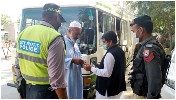 Two men speaking while standing in front of a bus, accompanied by a traffic constable and a policeman — Radio Pakistan