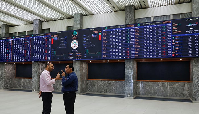 Two investors are involved in a conversation in front of the digital board at the Pakistan Stock Exchange. — Reuters/File