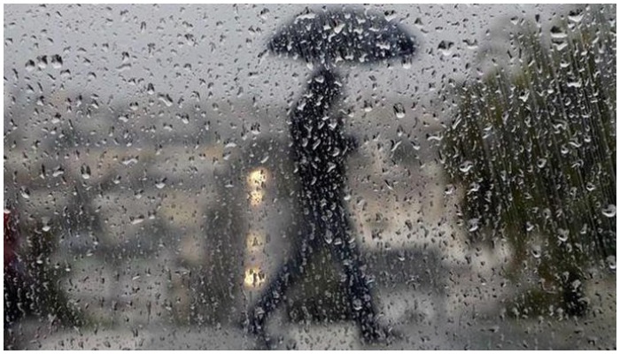 A man walks under an umbrella behind a glass screen covered with droplets of rain. Photo: Geo.tv/ file