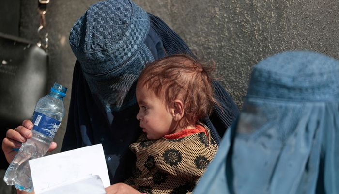 A displaced Afghan woman holds her child as she waits with other women to receive aid supply outside an UNCHR distribution centre on the outskirts of Kabul, Afghanistan October 28, 2021. — Reuters