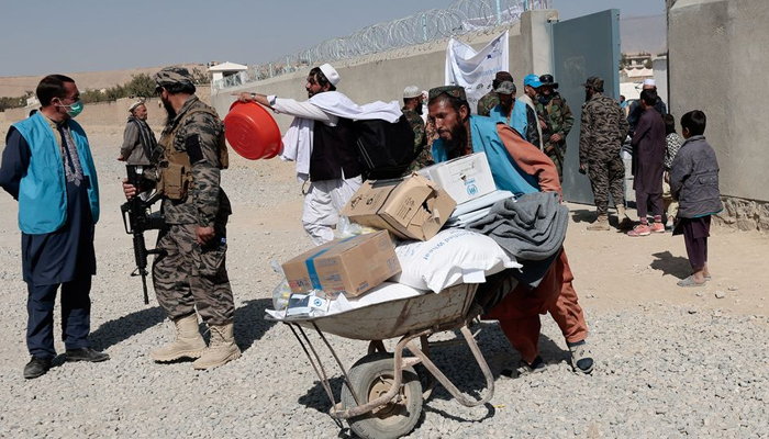 An UNHCR worker pushes a wheelbarrow loaded with aid supplies for a displaced Afghan family outside the distribution center as a Taliban fighter secures the area on the outskirts of Kabul, Afghanistan October 28, 2021. — Reuters