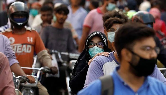 A woman wearing mask pillion rides with a man amid several other motorcycles on a road. Photo: Geo.tv/ file