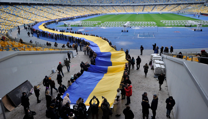 People carry a giant Ukraine´s national flag at a stadium to mark a Day of Unity in Kyiv on February 16, 2022. — AFP