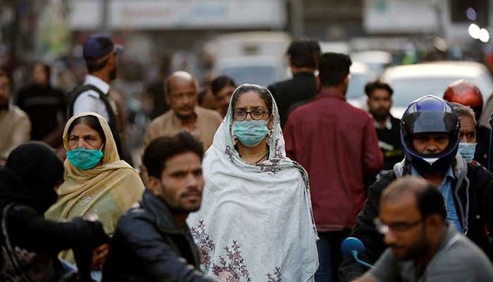 Two women wearing mask walk amid vehicles moving on a road. Photo: Geo.tv/ file