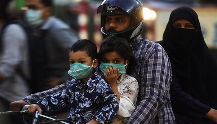 Two children wearing masks ride a motorcycle with their parents. Photo: site: Geo.tv