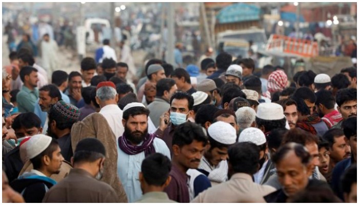 A man wearing mask talking on a mobile phone while walking among several others. Photo: Geo.tv/ file