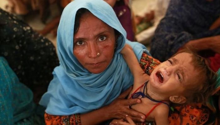 Image of Mah Pari carrying her son Gul Mir as she waits for her turn at the mobile feeding centre in Dera Murad Jamali. Photo: AFP
