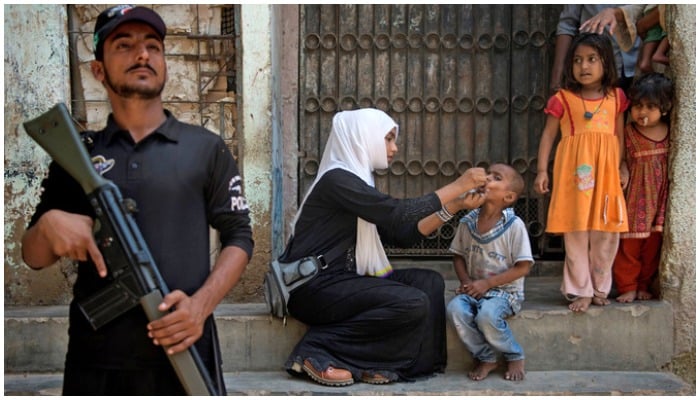 A cop stands guard as a health worker administers the polio vaccine to a child during a vaccination campaign in Karachi. Photo: AFP