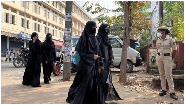 Hijab wearing schoolgirls arrive to attend their classes as a policewoman stands guard outside a government girls school after the recent hijab ban, in Udupi town in the southern state of Karnataka, India, February 16, 2022. Photo: Reuters/ file